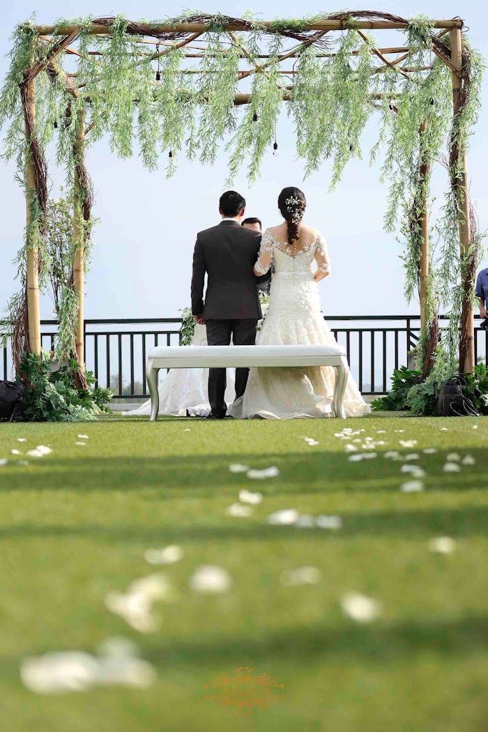 Elegant outdoor wedding ceremony with a couple under a floral arch in Indonesia.